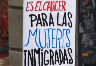 A woman holds a sign during a Barcelona demonstration on International Women's Day in 2009. The sign reads "Invisibility is the cancer for immigrant women." (Wikimedia Commons)