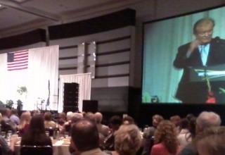 Ambassador Tony Hall gestures on the video screen during the 25th annual Colorado Prayer Luncheon. (Marrton Dormish)